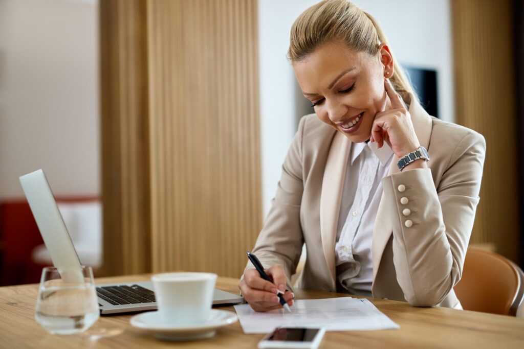 Colaboradora sorridente escrevendo relatórios enquanto trabalha em viagens corporativas